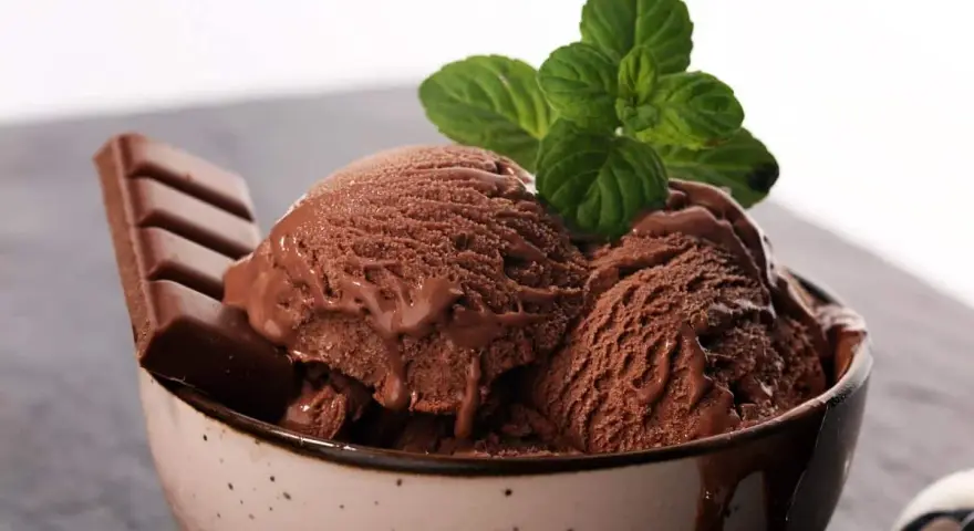 Delicioso helado de chocolate cremoso en un tazón, adornado con una hoja de menta y una barra de chocolate.