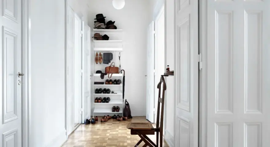 Ein heller, schmaler Flur wirkt optisch breiter durch weiße Türen und eine offene Regalwand mit Schuhen und Accessoires.