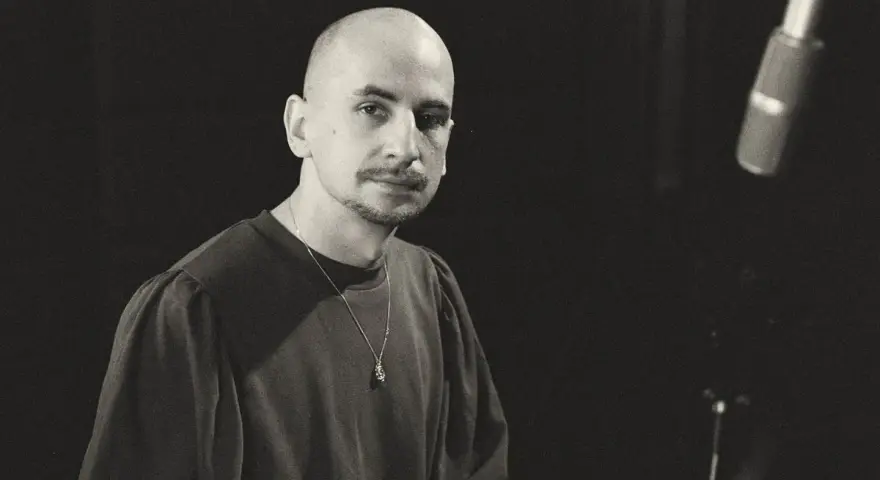 Marek Pędziwiatr, z charakterystyczną łysą głową i wąsikiem, w ciemnej bluzie i z naszyjnikiem, przygotowuje się do nagrania.