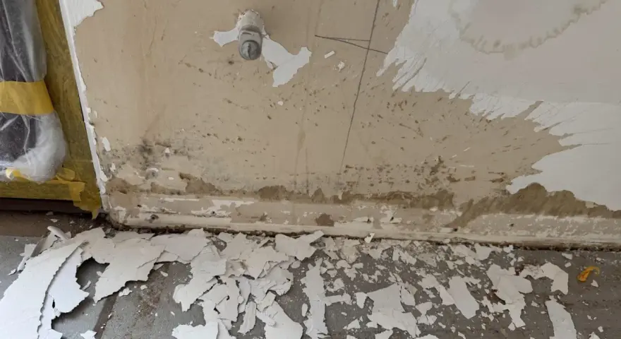 Vorbereitung zum zumauern einer Heizungsnische: abgeplatzter Putz und Schmutz am Boden, Wand mit Wasserflecken und einem Ventil.