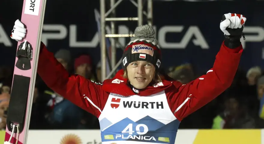 Skoczek narciarski w czerwonej kurtce i czapce z polską flagą świętuje zwycięstwo na skoczni. Mistrzostwa świata w skokach narciarskich.