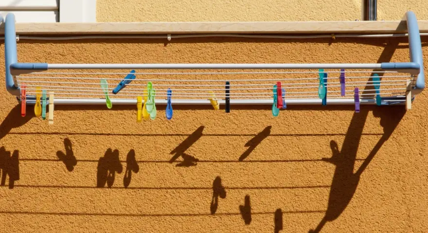 Variados tipos de tendederos exteriores con pinzas de colores sujetan la ropa. Las sombras proyectadas crean un patrón interesante sobre la pared texturizada.