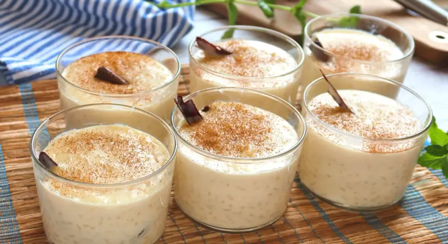 Seis vasitos de cremoso arroz con leche, espolvoreados con canela y decorados con una ramita de canela.