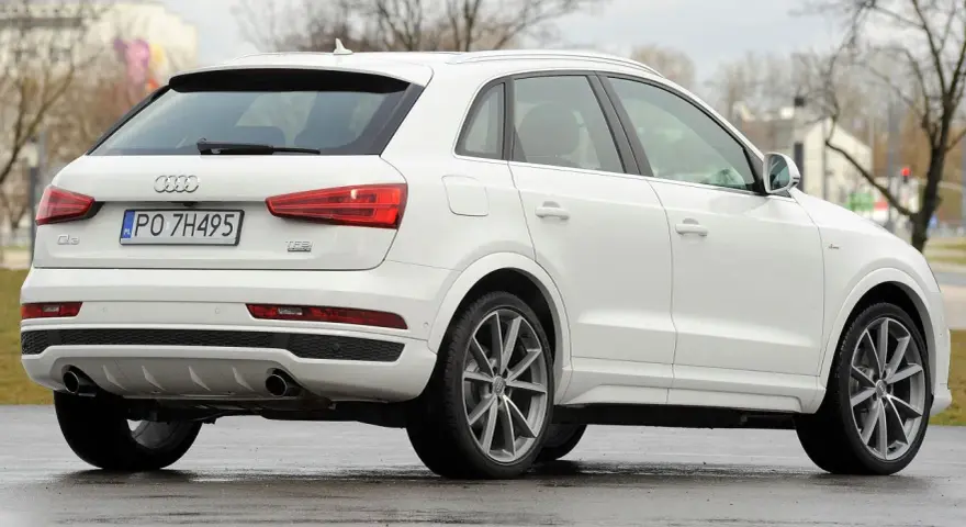 Biały SUV Audi Q3, idealny suv do 70 tys. zł, z polskimi tablicami rejestracyjnymi PO 7H495, widoczny z tyłu i z boku.