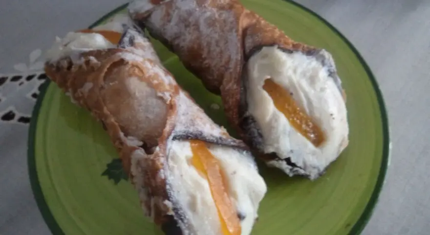 Dwa pyszne cannoli z kremem i kandyzowaną skórką pomarańczową, posypane cukrem pudrem. Ten makaron to prawdziwa rozkosz!
