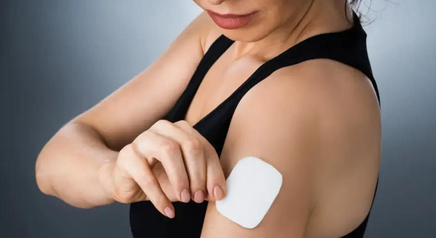 Kobieta przykleja plaster antykoncepcyjny na ramię. Dyskretny sposób na kontrolę płodności.