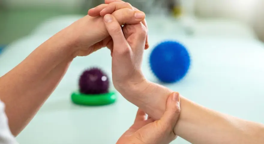 Fizjoterapeuta pomaga pacjentowi w ćwiczeniach na palec trzaskający, używając masażu i piłeczek do rehabilitacji.