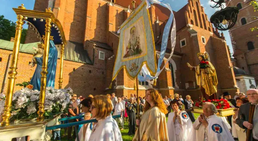 Prozession mit Marienstatue und Fahne vor einer Kirche. Menschen in weißen Gewändern, ein Festtag in Polen.