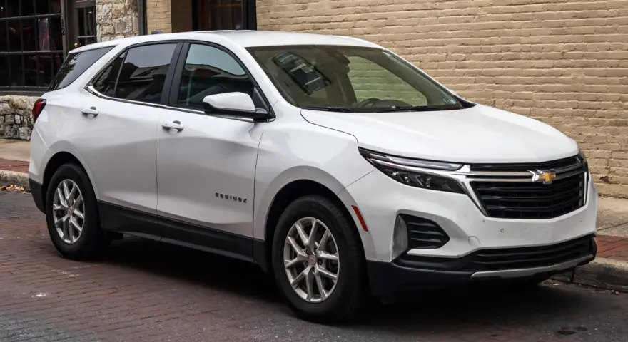 Biały Chevrolet Equinox stoi zaparkowany na brukowanej ulicy, obok ceglanego budynku.