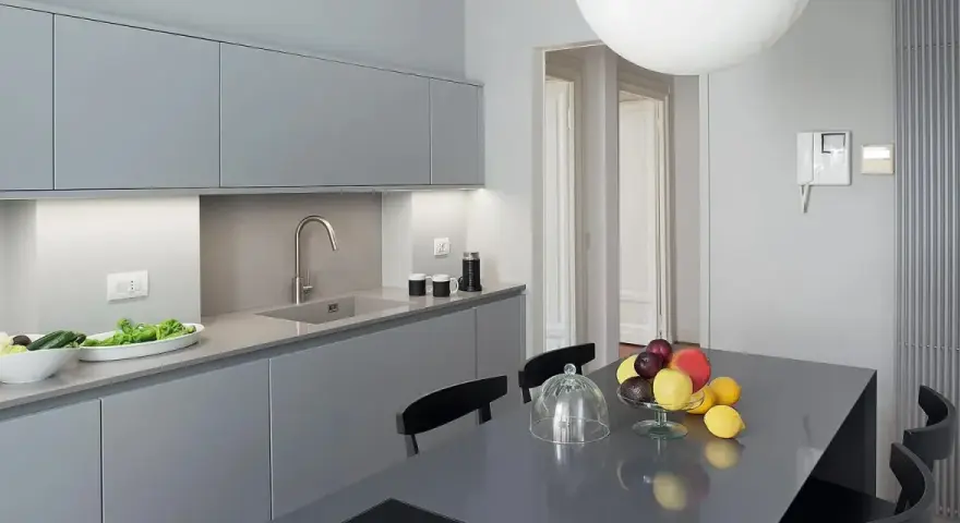 Cucina moderna con pensili e basi grigie. Il colore pareti neutro esalta la pulizia delle linee. Tavolo con frutta fresca.