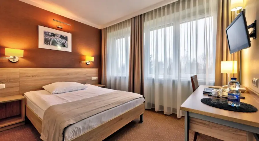 Przytulny pokój hotelowy w Białymstoku z wygodnym łóżkiem, biurkiem i telewizorem.