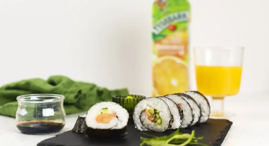 Pyszne sushi z łososiem, ogórkiem i ryżem, podane z sosem sojowym i sokiem pomarańczowym.