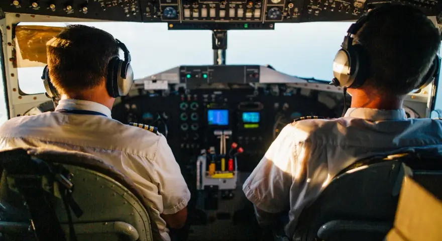 Dwóch pilotów samolotu w słuchawkach na tle kokpitu.
