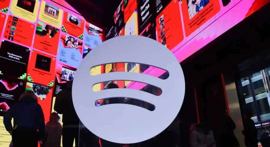 Duże logo Spotify na tle ekranów z podsumowaniami słuchania, w tym informacją o najpopularniejszym artyście na Spotify.