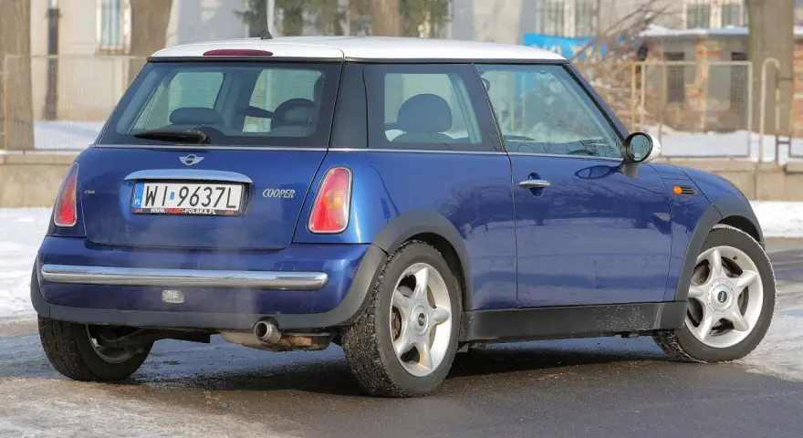 Niebieski Mini Cooper R50 z białym dachem, zaparkowany na zaśnieżonej drodze.