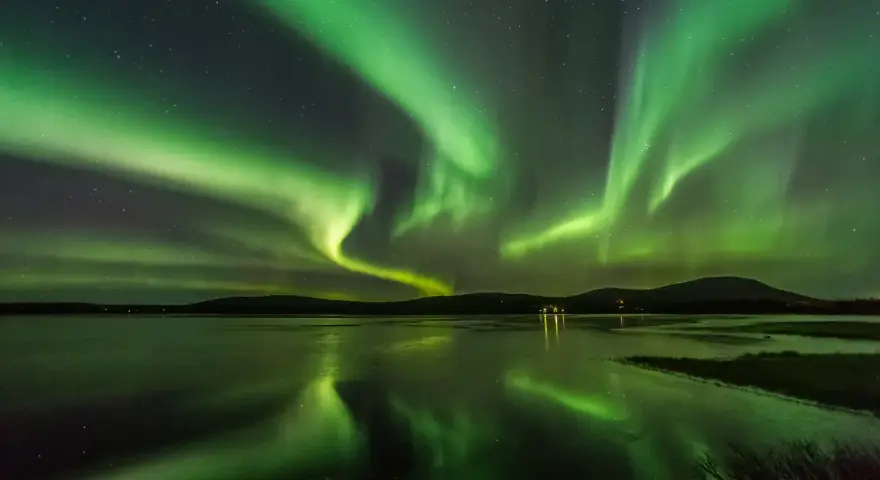 Grönt norrsken dansar över en frusen sjö i Finland. Stjärnor lyser på himlen och speglar sig i vattnet.