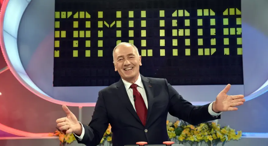 Uśmiechnięty prowadzący w garniturze na tle planszy z zielonymi polami, jak w Familiadzie. Ile lat ma ten program?