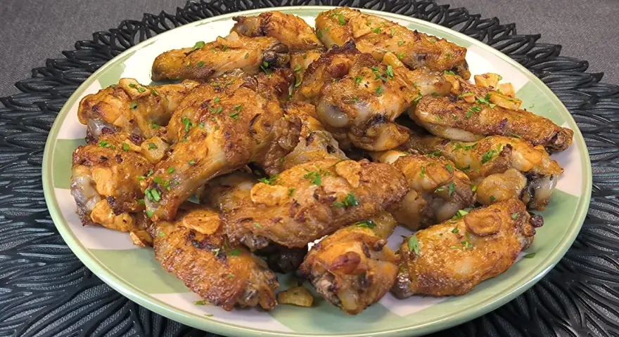 Alitas de pollo doradas con ajo y perejil en un plato verde.