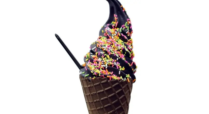 Schwarzes Eis in einer Waffel, bestreut mit bunten Streuseln. Ein schwarzer Löffel steckt darin.