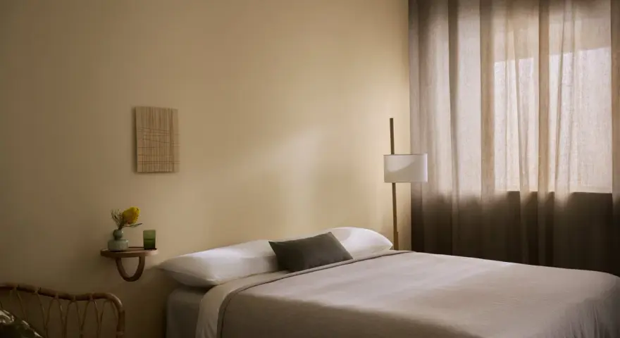 Ett lugnt sovrum med beige väggar, en bekväm säng och en golvlampa. Perfekt för att måla sovrum i en avkopplande stil.
