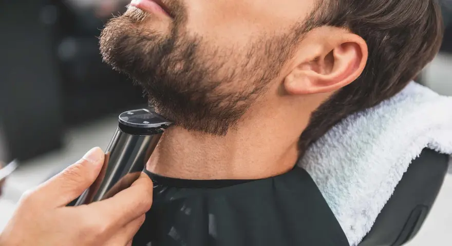 Barbero perfilando barba con recortadora, creando diseños de barba modernos.