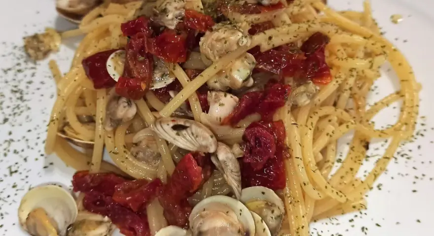 Spaghetti con lupini e pomodorini secchi, un piatto di mare saporito e profumato, guarnito con prezzemolo tritato.