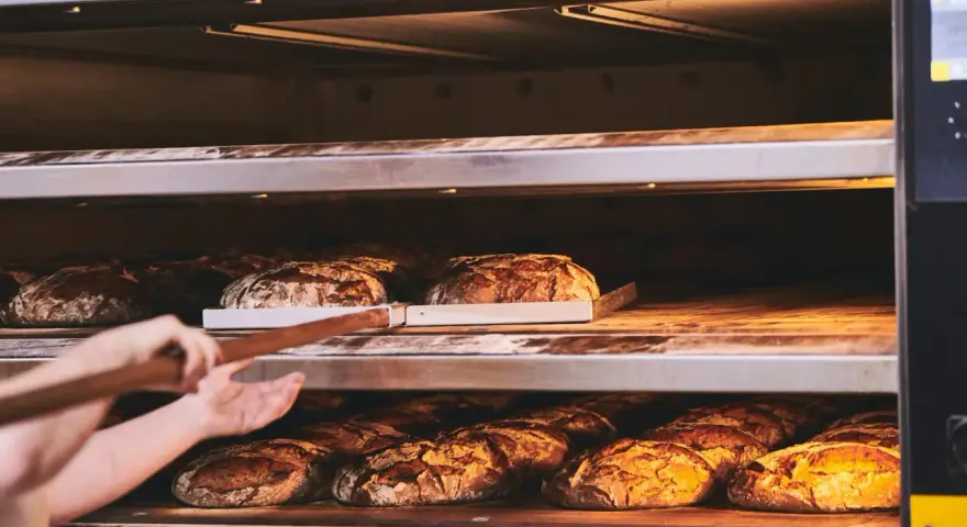 Bäcker lässt den **backofen spalt offen lassen beim backen** für knuspriges Brot. Mehrere Brote auf Regalen im Ofen.