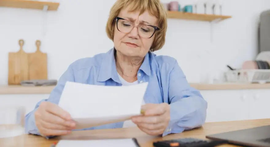 Kobieta w wieku 60 lat, po 40 latach pracy, z troską przegląda dokumenty dotyczące emerytury.