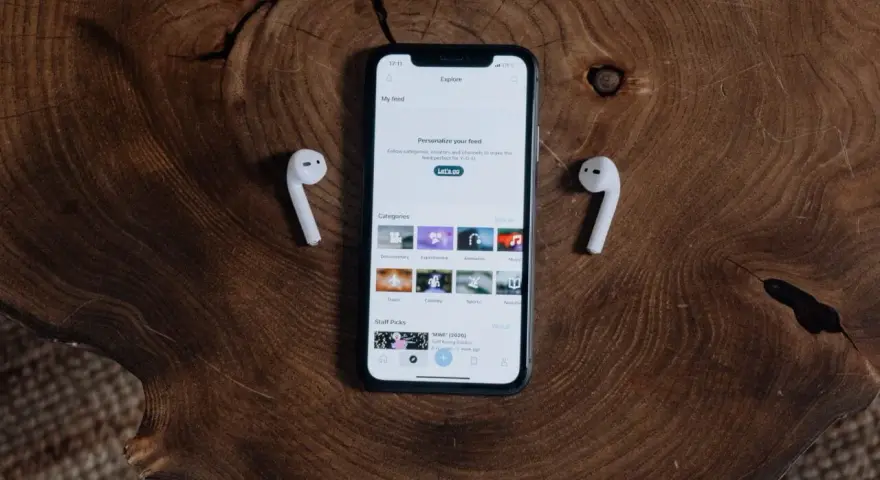 iPhone z AirPods na drewnianym tle.