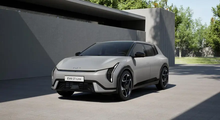 Nowoczesny, jasnoszary Kia EV4 GT-Line stoi na podjeździe przed minimalistycznym budynkiem.
