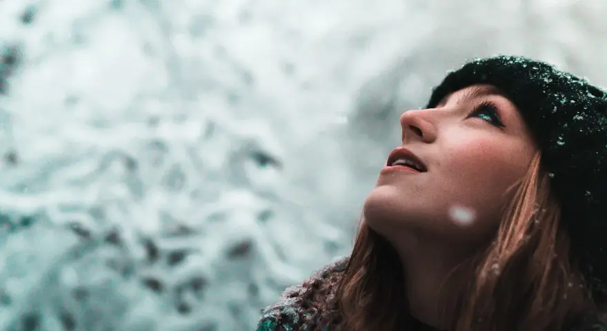 Junge Frau blickt in den Schnee, ihre Wangen gerötet, ein Zeichen von trockene Haut im Winter.
