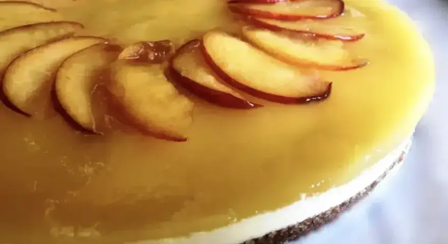 Cheesecake alla pesca con fette di pesca fresca disposte a raggiera sulla glassa gialla.