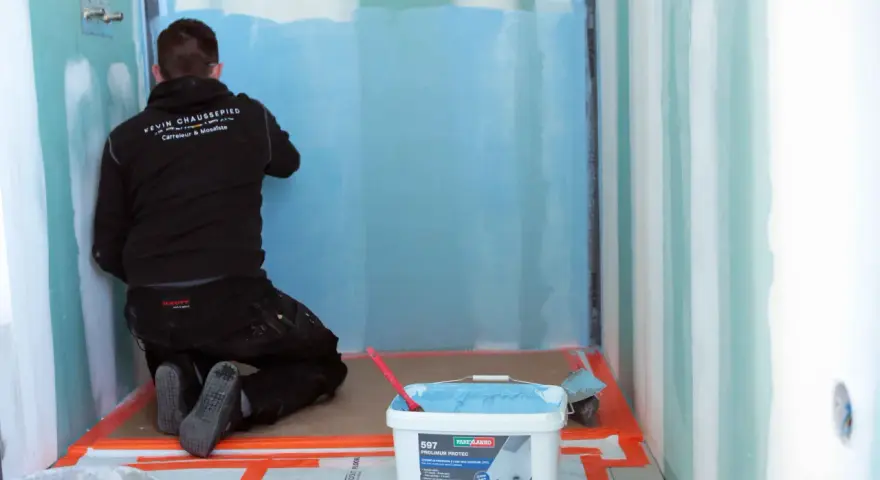 Un carreleur applique une protection étanche avant la pose carrelage dans une douche.