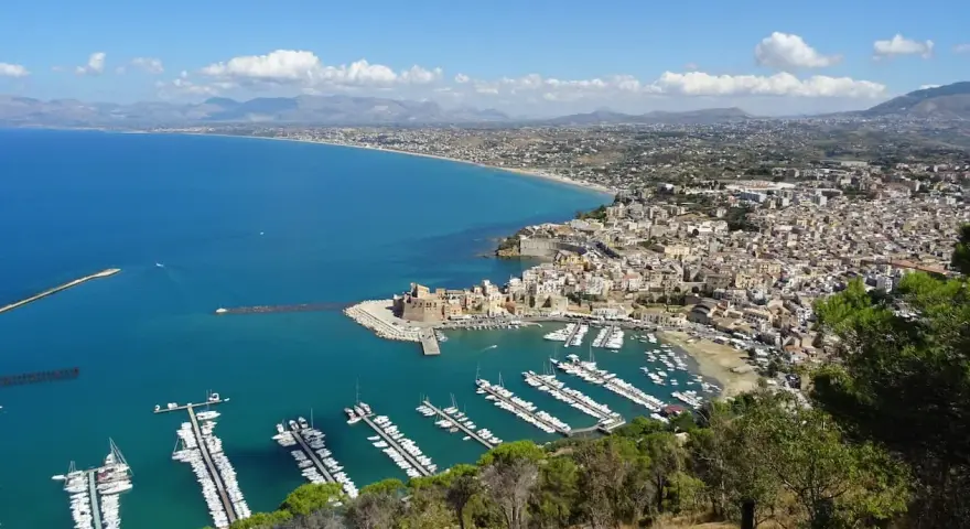 Vista panoramica di Castellammare del Golfo, con il castello, il porto turistico pieno di barche e la costa siciliana.