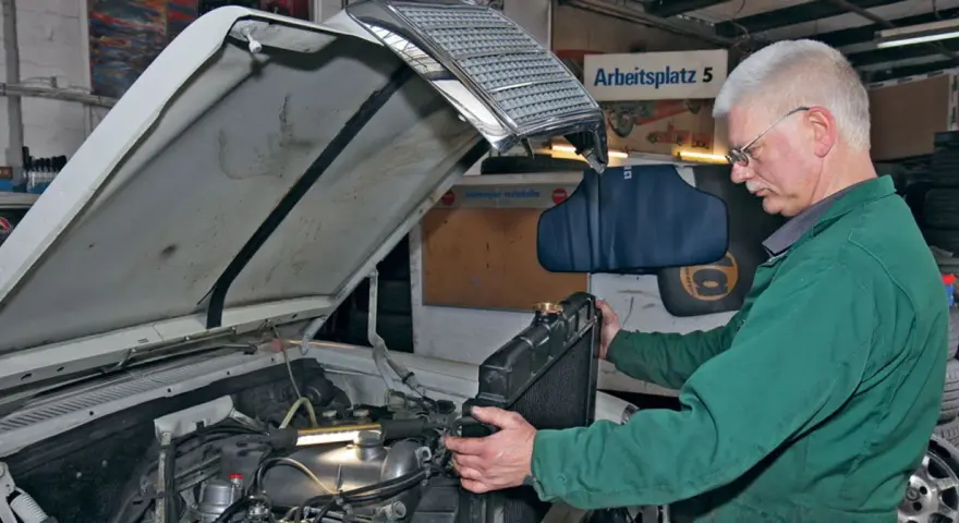Mechanik w zielonym kombinezonie wykonuje wymianę chłodnicy krok po kroku w warsztacie.