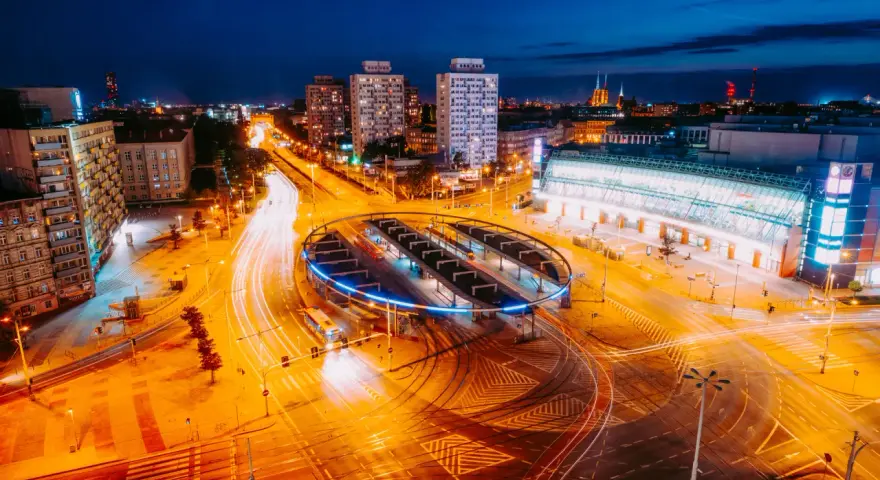 Widok z lotu ptaka na nocne miasto z długimi smugami świateł samochodowych i tramwajowych.