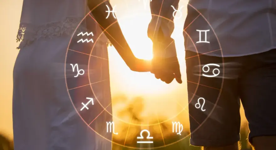 Para, trzymająca się za ręce, na tle zachodzącego słońca, otoczona kołem zodiaku, gdzie widać symbole Lwa i Koziorożca.