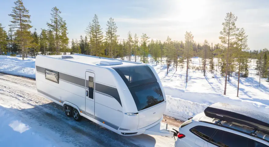 Vit husvagn dras av bil genom snöig skog. Den bästa husvagnen för äventyr nära Haparanda.