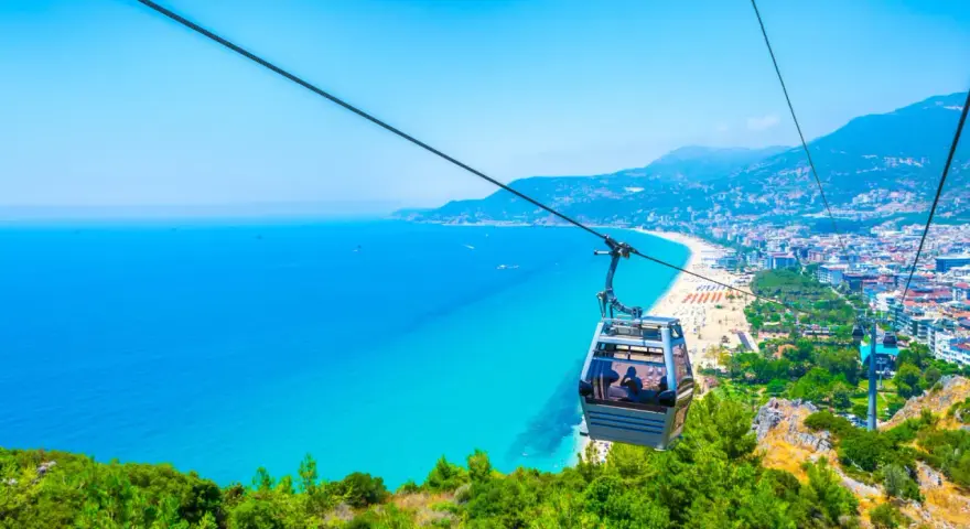 Kolejka linowa nad turkusowym morzem i plażą w Alanyi. Widok z góry na miasto i wybrzeże. Czy Alanya jest bezpieczna? Tak, wygląda na spokojną i piękną.
