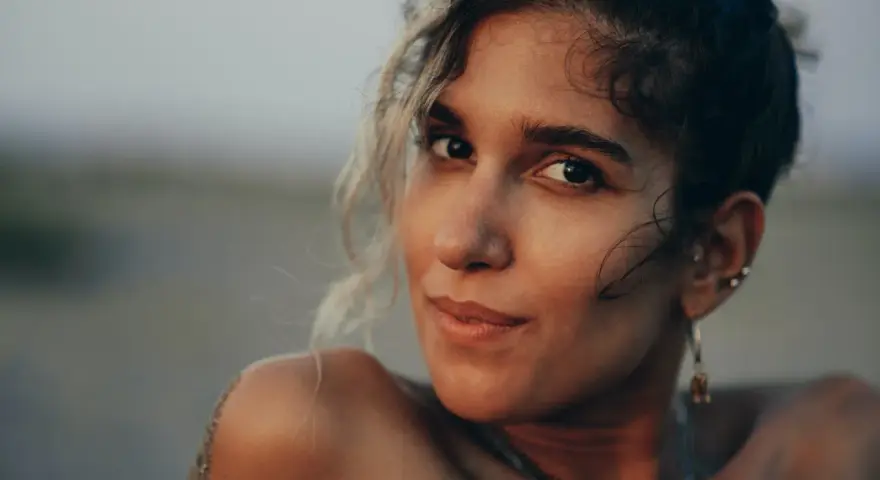 Photos de portrait d'une jeune femme aux cheveux bouclés, le sable sur son épaule, regardant la caméra avec un léger sourire.