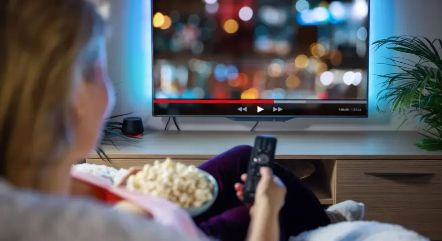Persona relajada viendo una serie en francés en la televisión, con palomitas y mando a distancia.