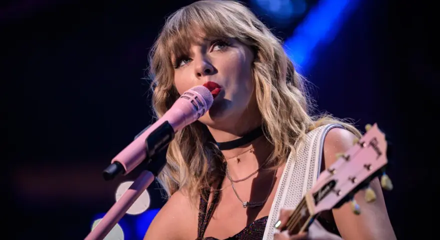 Taylor Swift śpiewa do różowego mikrofonu, grając na gitarze. To scena z jej epickiej trasy "reputation stadium tour", która na zawsze zmieniła jej wizerunek.