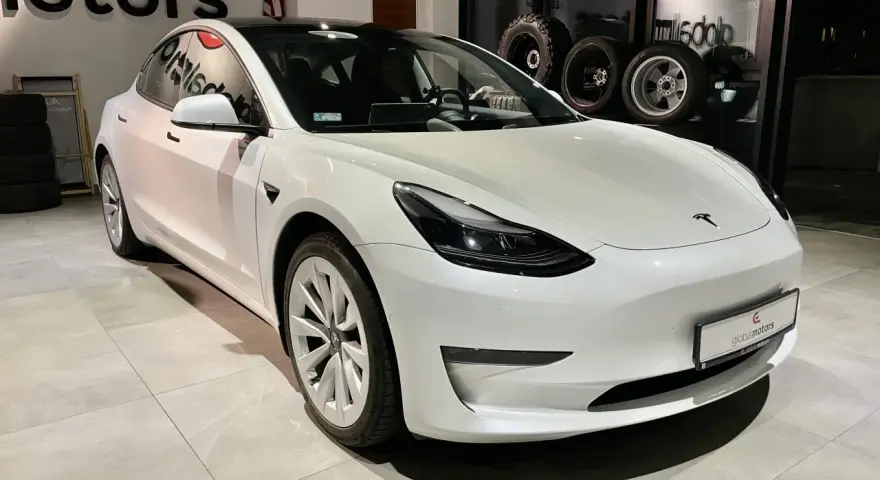 Biała Tesla Model 3 z napędem na cztery koła stoi w salonie samochodowym.