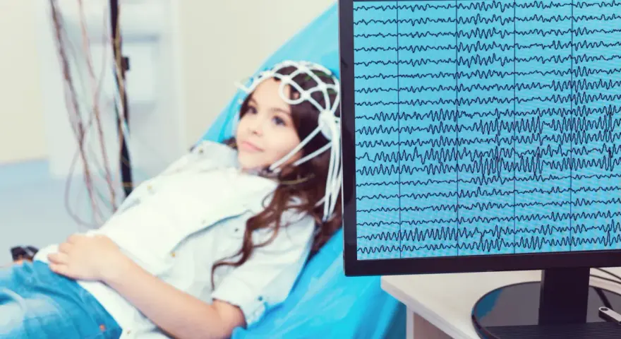 Dziewczynka z czepkiem EEG leży na kozetce, a na monitorze widać zapis fal mózgowych. Badanie pomaga zrozumieć zespół Aspergera a wynik EEG.