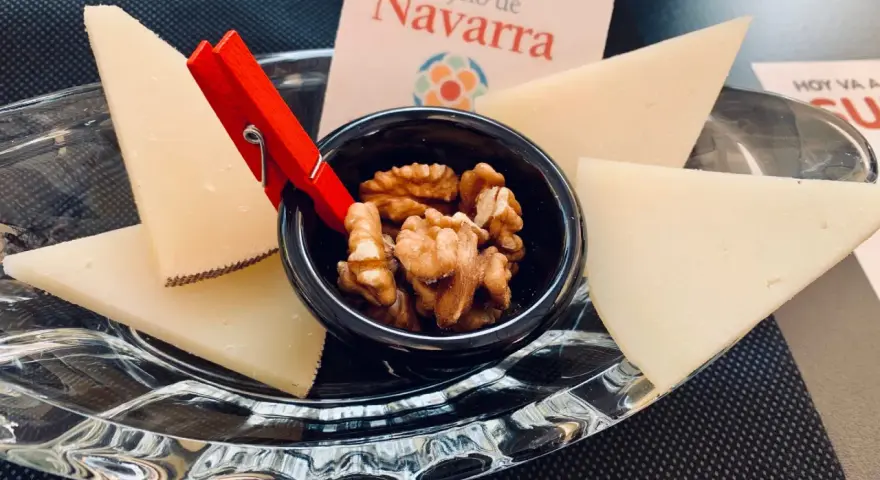 Queso en cuñas con nueces en un cuenco negro, sobre plato de cristal y tarjeta "Reino de Navarra".