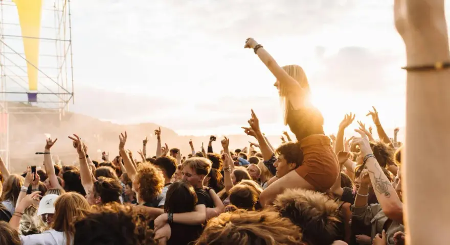 Menschen jubeln auf einem Festival in Rostock. Eine Frau sitzt auf den Schultern eines anderen Besuchers, während die Sonne untergeht.