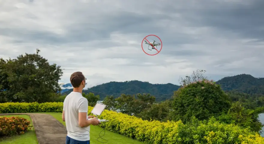 Man with drone controller looks at a drone with a "no fly" symbol, illustrating ct drone laws.