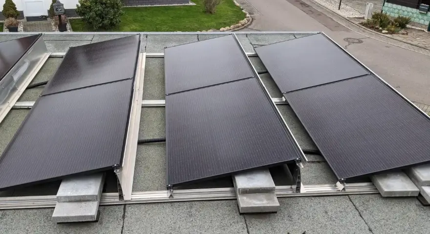 Solarmodule auf einem Bitumen-Flachdach, befestigt mit einer Aufständerung. Ein kleiner schwarzer Kater beobachtet die Installation.