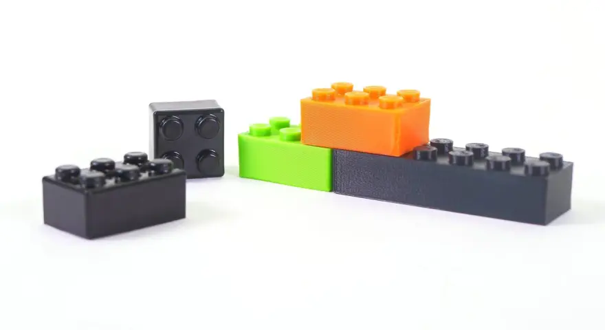 Klocki z drukarki 3D, wykonane z materiału ABS, w kolorach czarnym, zielonym i pomarańczowym, ułożone na białym tle.
