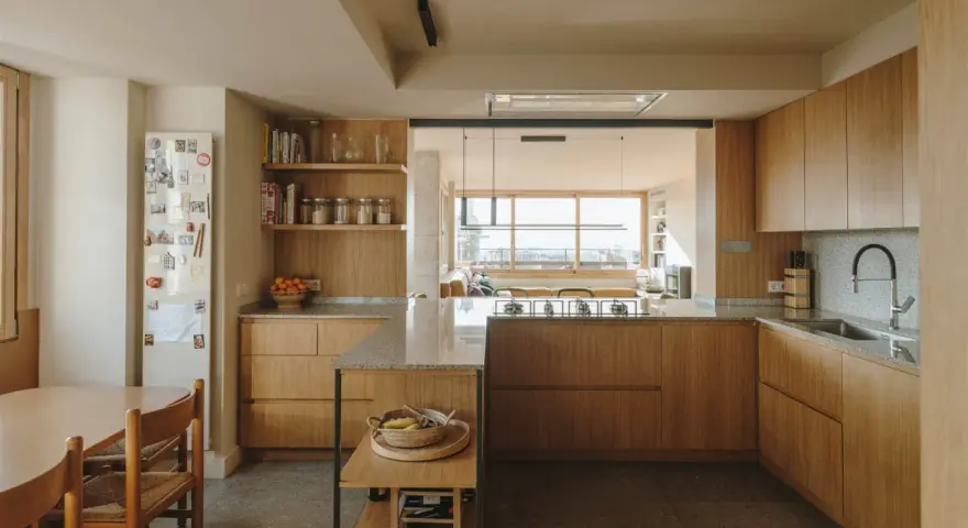Cocinas color madera con encimeras de granito, electrodomésticos integrados y una isla central. Un comedor adyacente con mesa y sillas de madera.
